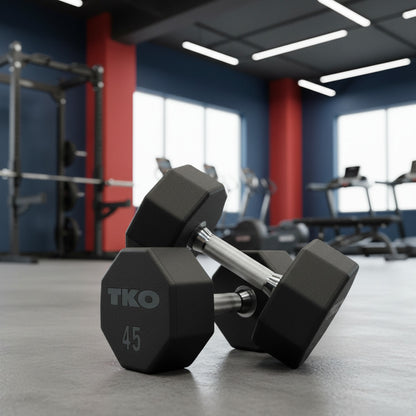 Pair of TKO dumbbells on a gym floor with equipment in the background.