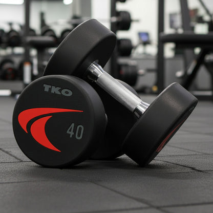 Pair of TKO 830US Signature Urethane Dumbbells shown in a gym setting.