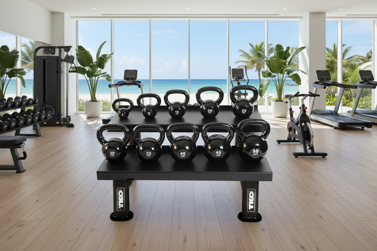 Set of TKO 859KR-857KBV-BK kettlebells on a platform with a view of the ocean through large windows.